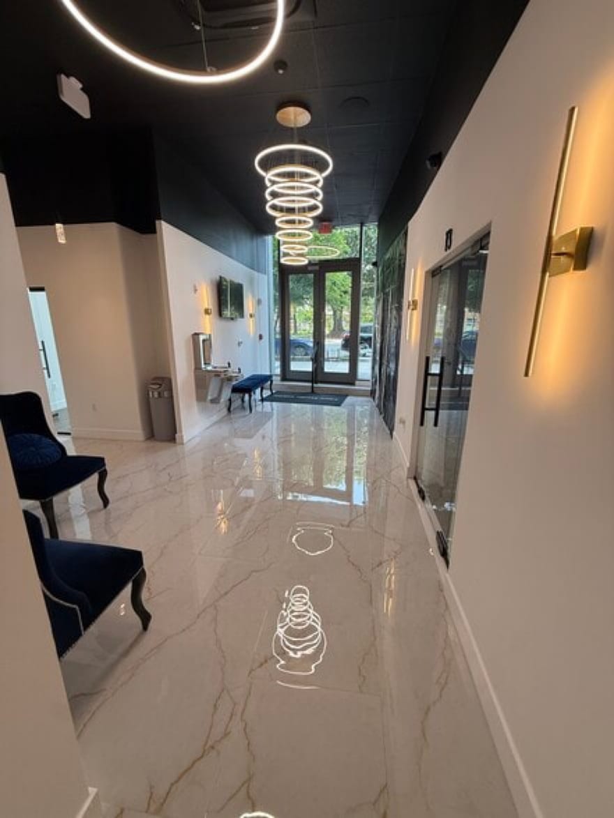 The entry at 7917-B Westpark Drive: polished marble underfoot, a spiral ring chandelier overhead, brass wall sconces, navy velvet seating and the glass doors out to the parking lot.