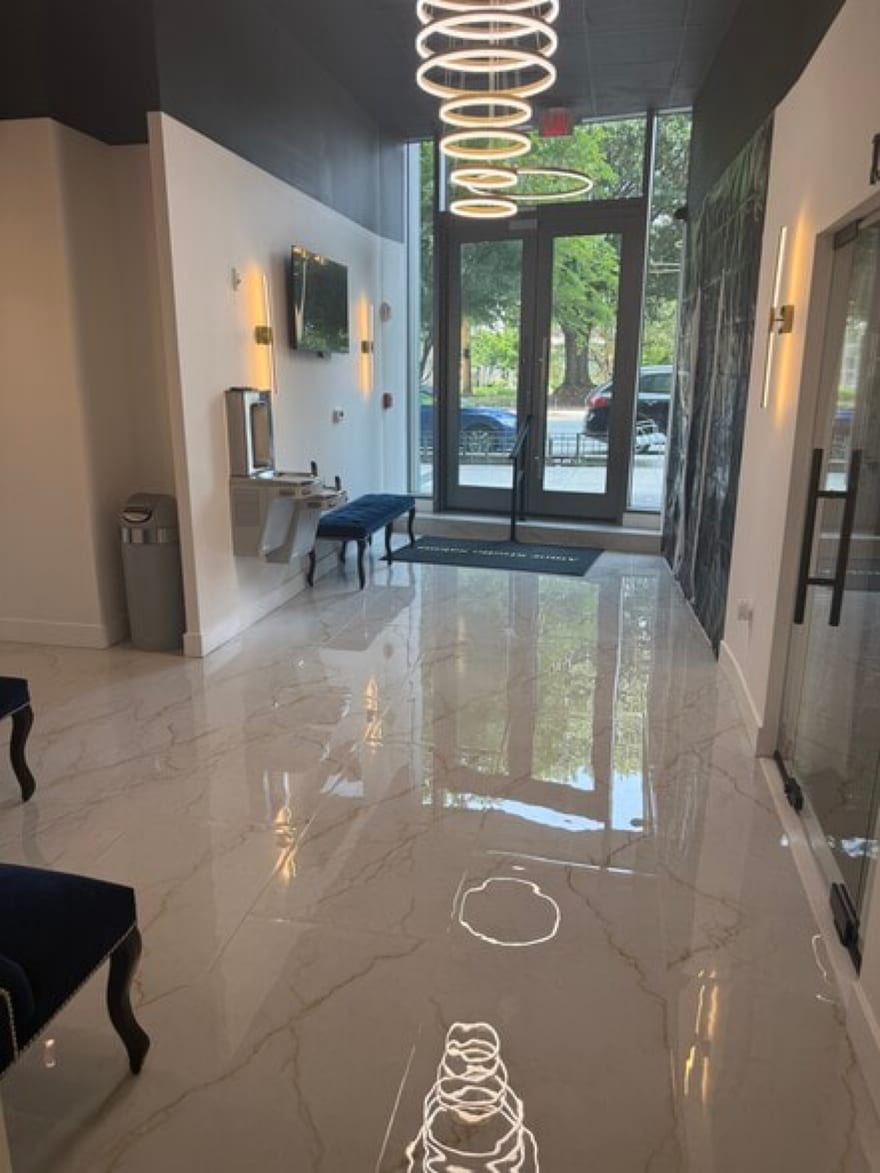 The lobby at the Tysons building looking back to the glass doors: polished marble underfoot, a spiral ring chandelier overhead, brass sconces and navy velvet seating.
